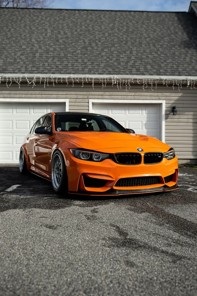 BMW F80 M3 wrapped in gloss orange parked in front of a garage