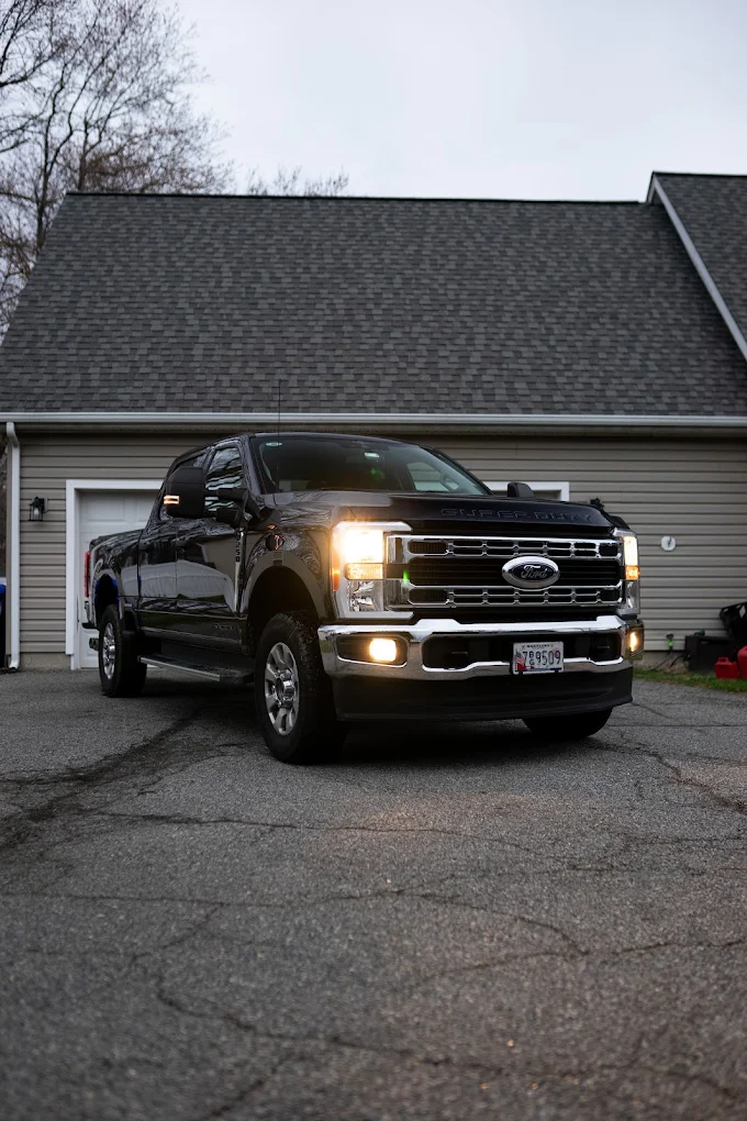 Detailed black Ford F-250 Super Duty with headlights on in a driveway